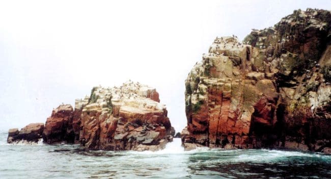 Natural rock arch and reddish cliffs at the Ballestas Islands in Paracas, Peru