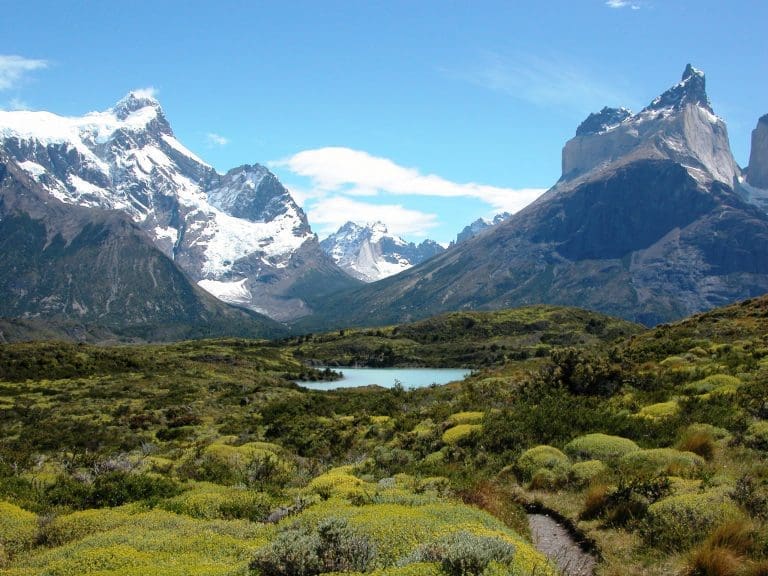 A panoramic view of the Torres del Paine mountains across a small lake and gorgeous bright green vegetation