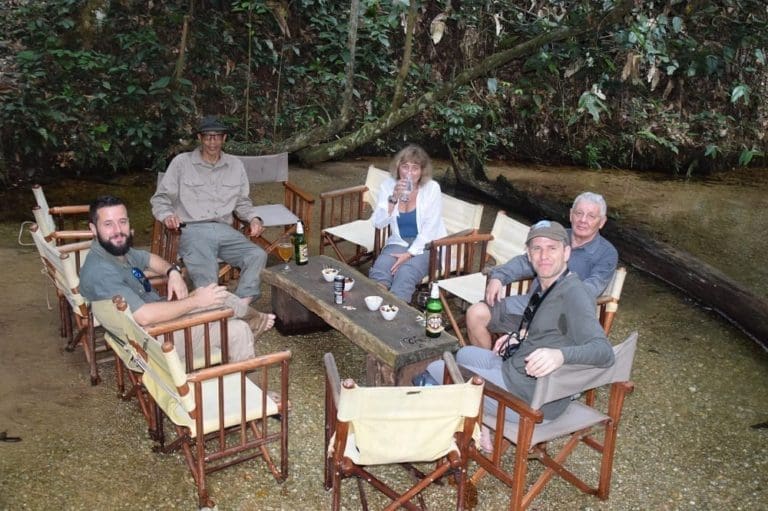 Sue, Clem and guests drinking at a table set in the river, Odzala,