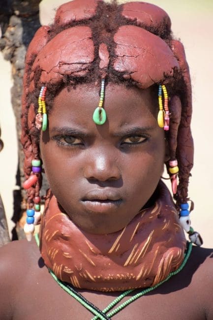 Angola - Headshot of young Muila lady with decorated mud coloured hair and necklaces Angola